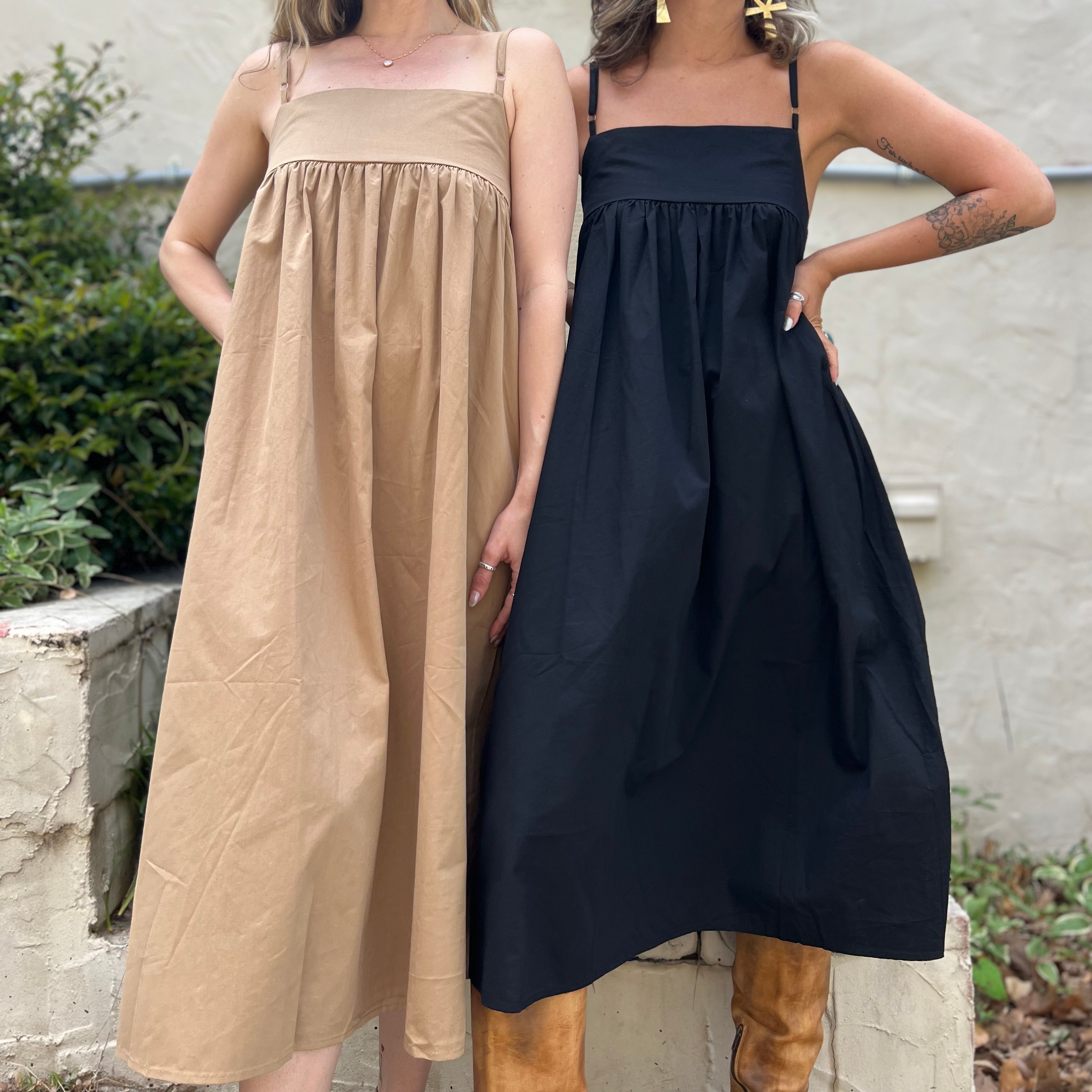 Two women wearing the Solid Color Pleats Suspender Acetate Fiber Free Size Dresses in black and khaki in front of a white wall with greenery.