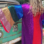 A woman wearing the Vintage Rainbow Sequin Striped Long Kimono with a black dress in front of a vintage teal Volkswagen bus, showing off the back.