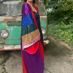 A woman wearing the Vintage Rainbow Sequin Striped Long Kimono with a black dress in front of a vintage teal Volkswagen bus, showing off the side.