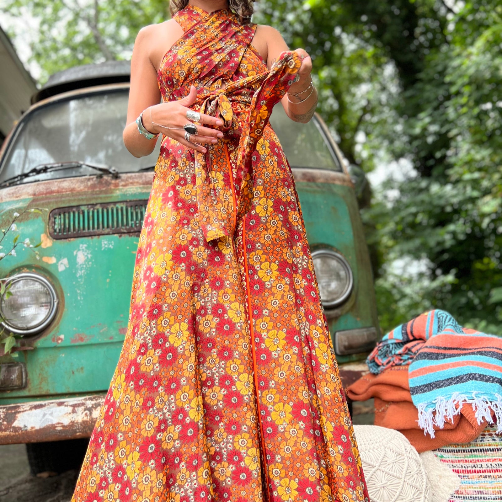 Woman in a colorful dress standing in front of a vintage van with greenery in the background