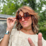 A woman wearing the tortoise Iris Seventies Hexagon Sunglasses with a cream top.