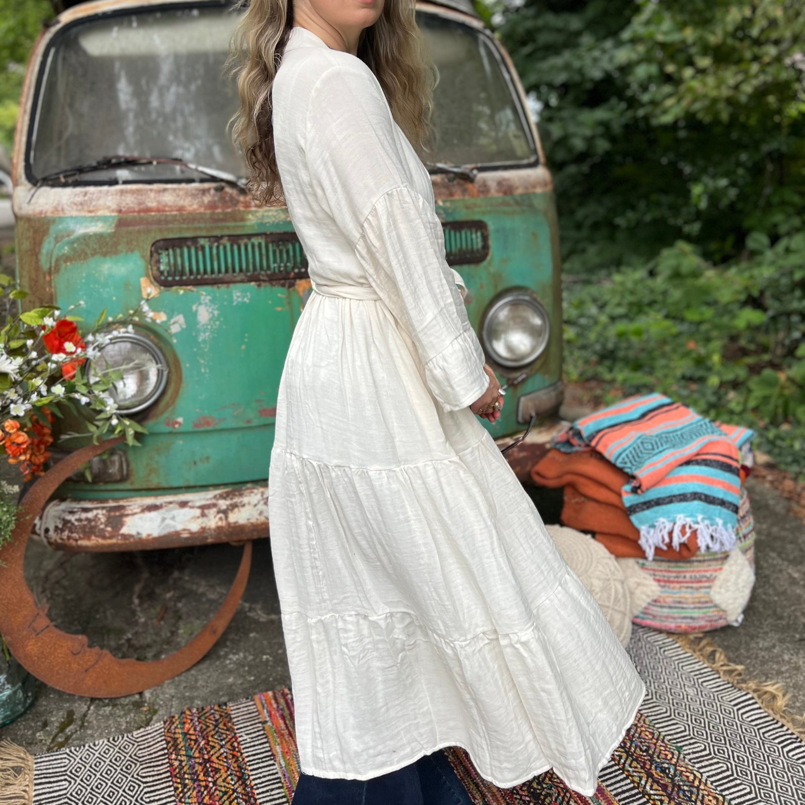 A woman wearing the white Organic Tiered Maxi Kimono Wrap Dress in front of a vintage Volkswagen bus.
