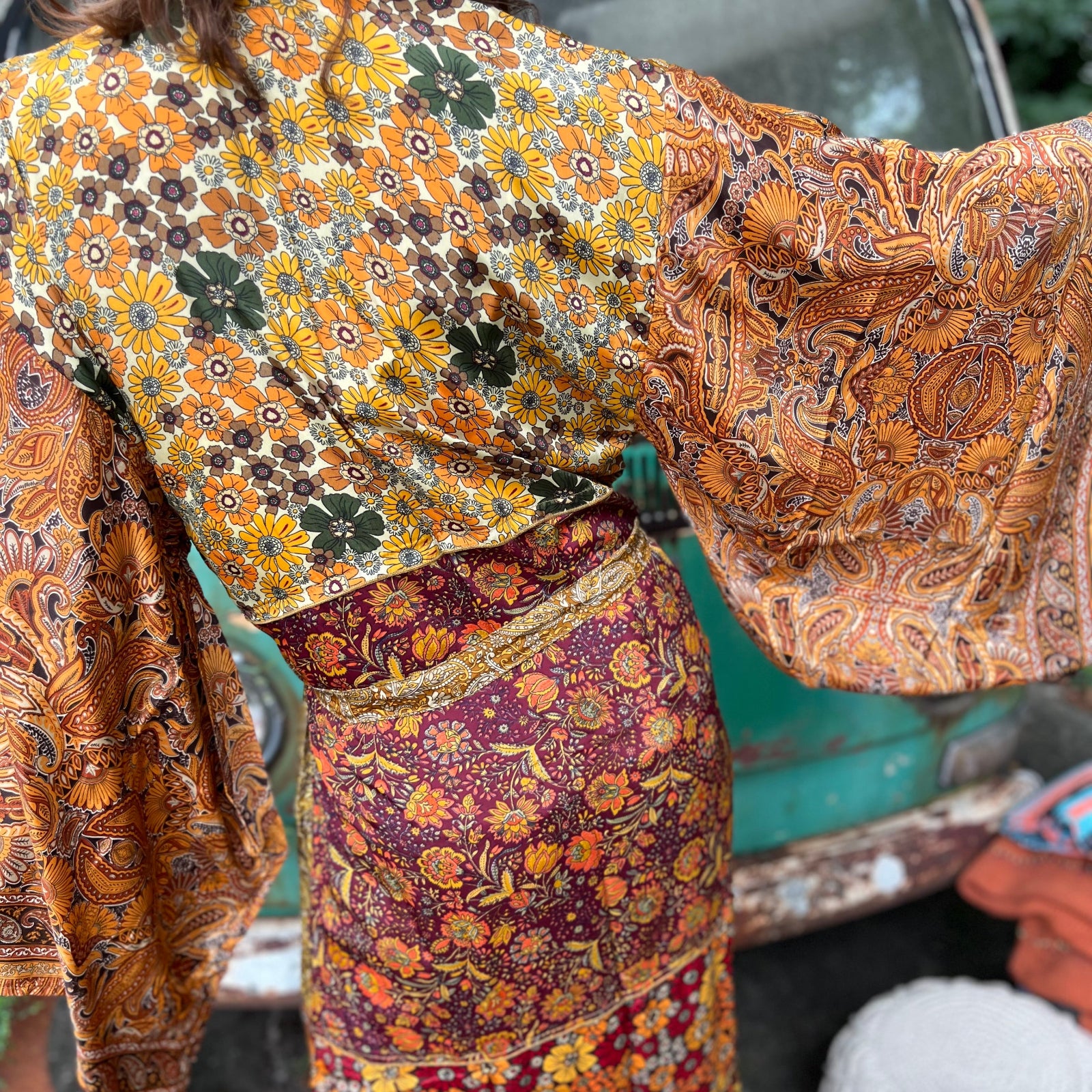 A woman the Hippie Golden Patchwork Kimono Robe Duster with a white bralette and red velvet bellbottoms in front of a vintage Volkswagen bus.