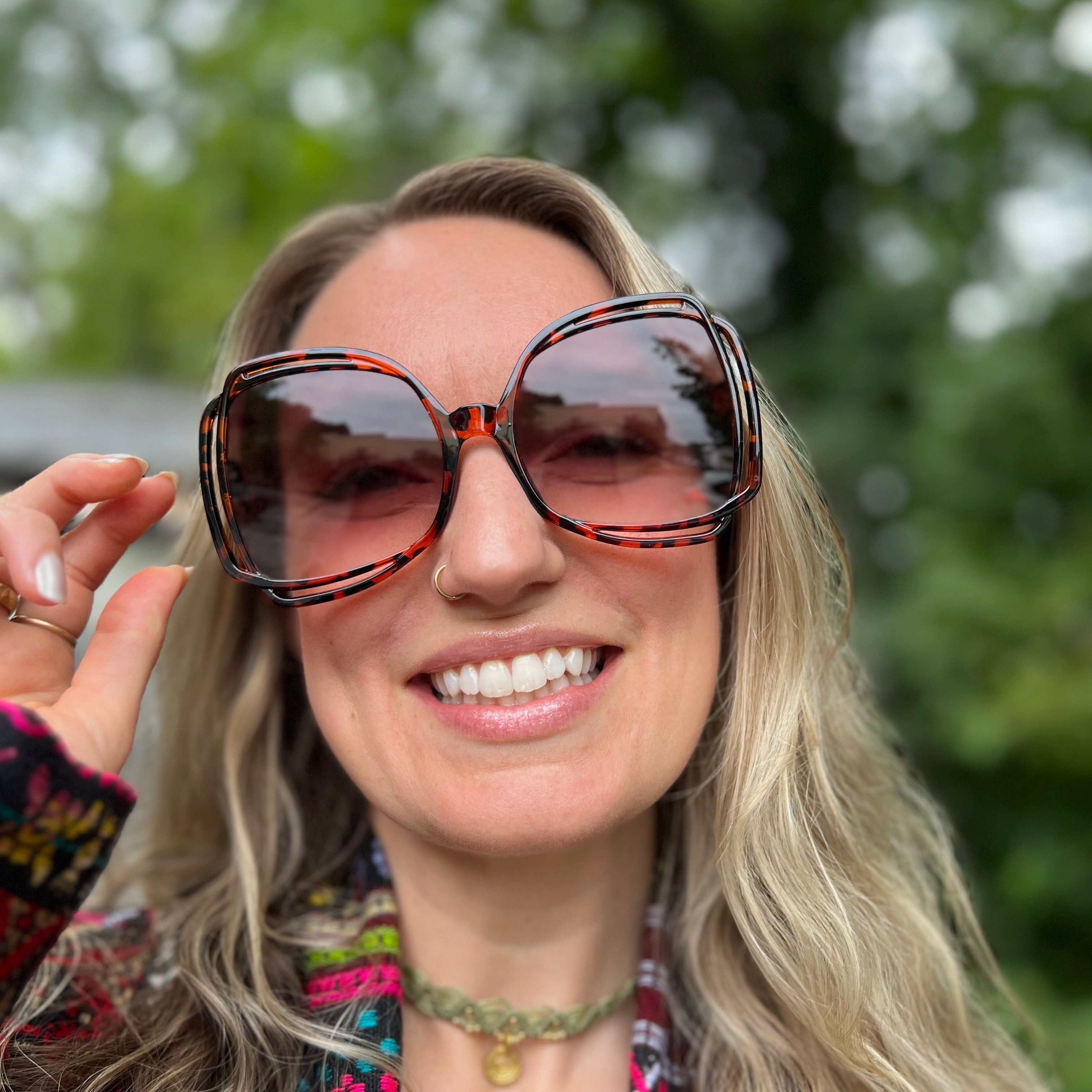 A woman wearing the turquoise Sofia Sunglasses with a colorful jacket.