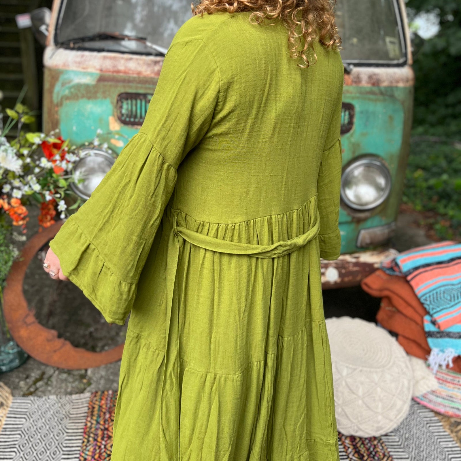 A woman wearing the golden Cyprus green Organic Tiered Maxi Kimono Wrap Dress in front of a vintage Volkswagen bus.