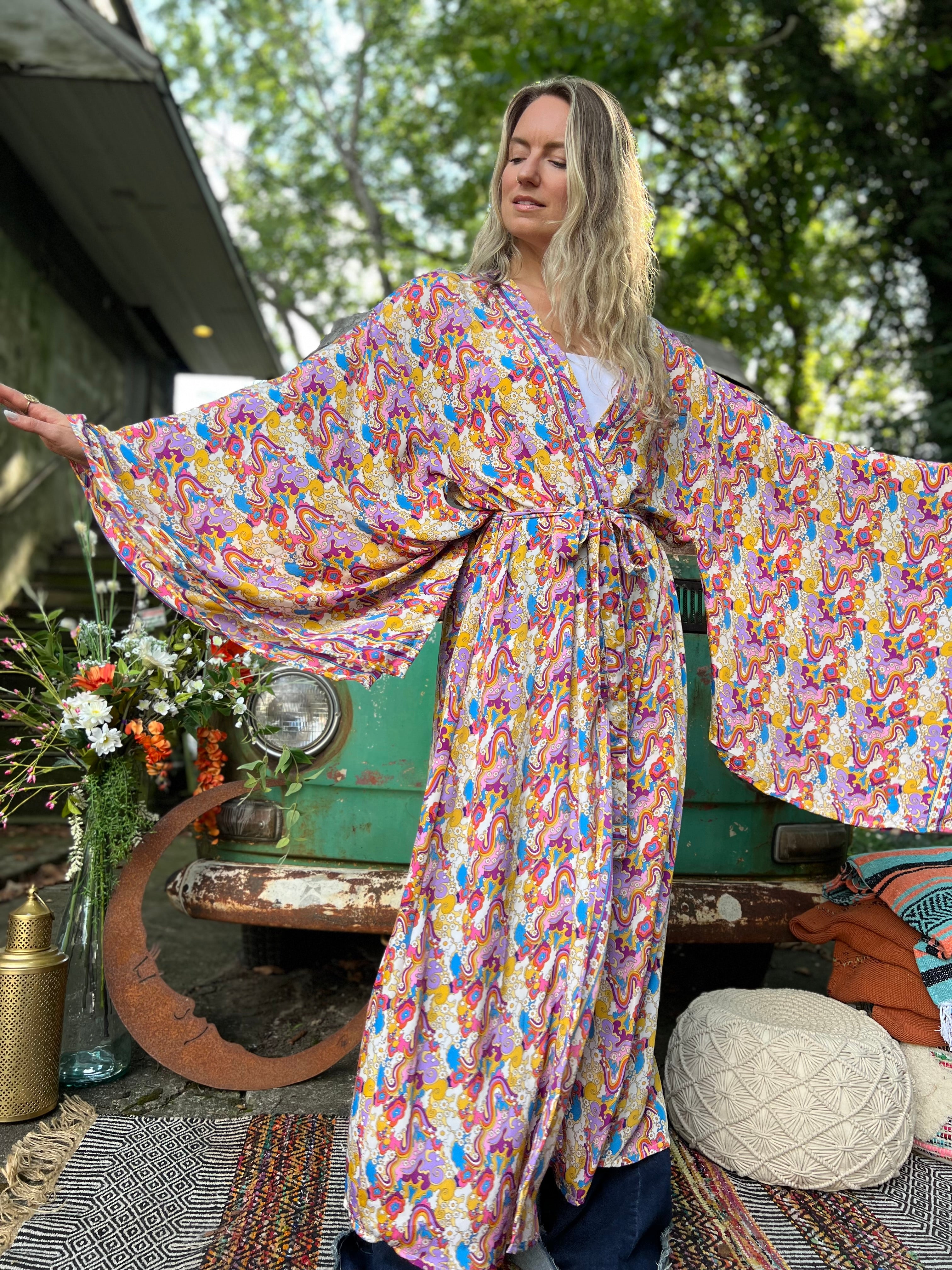 A woman wearing the Rainbow Hippie Boho Psychedelic Kimono Robe in front of a vintage Volkswagen bus.