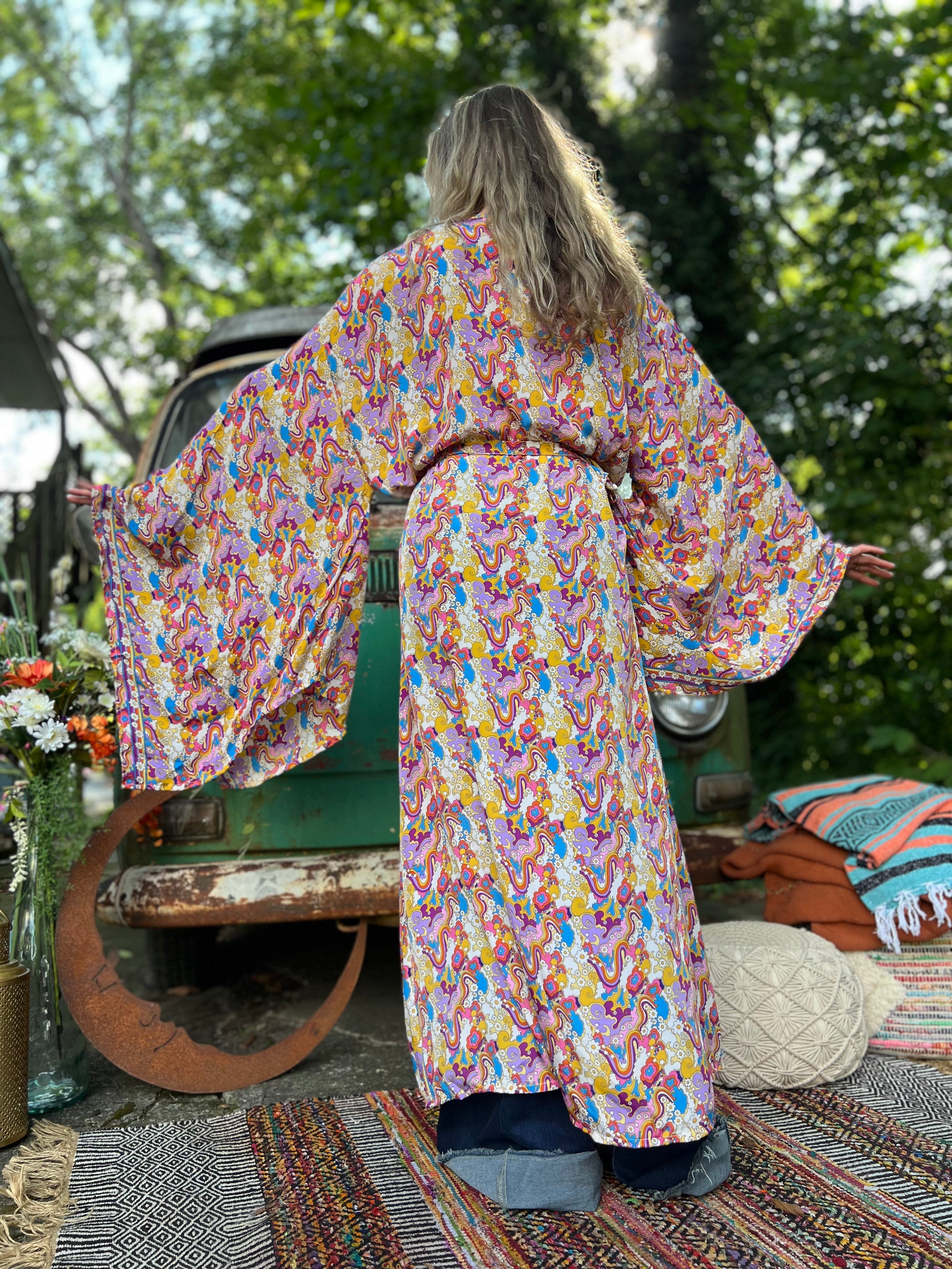 A woman wearing the Rainbow Hippie Boho Psychedelic Kimono Robe in front of a vintage Volkswagen bus.