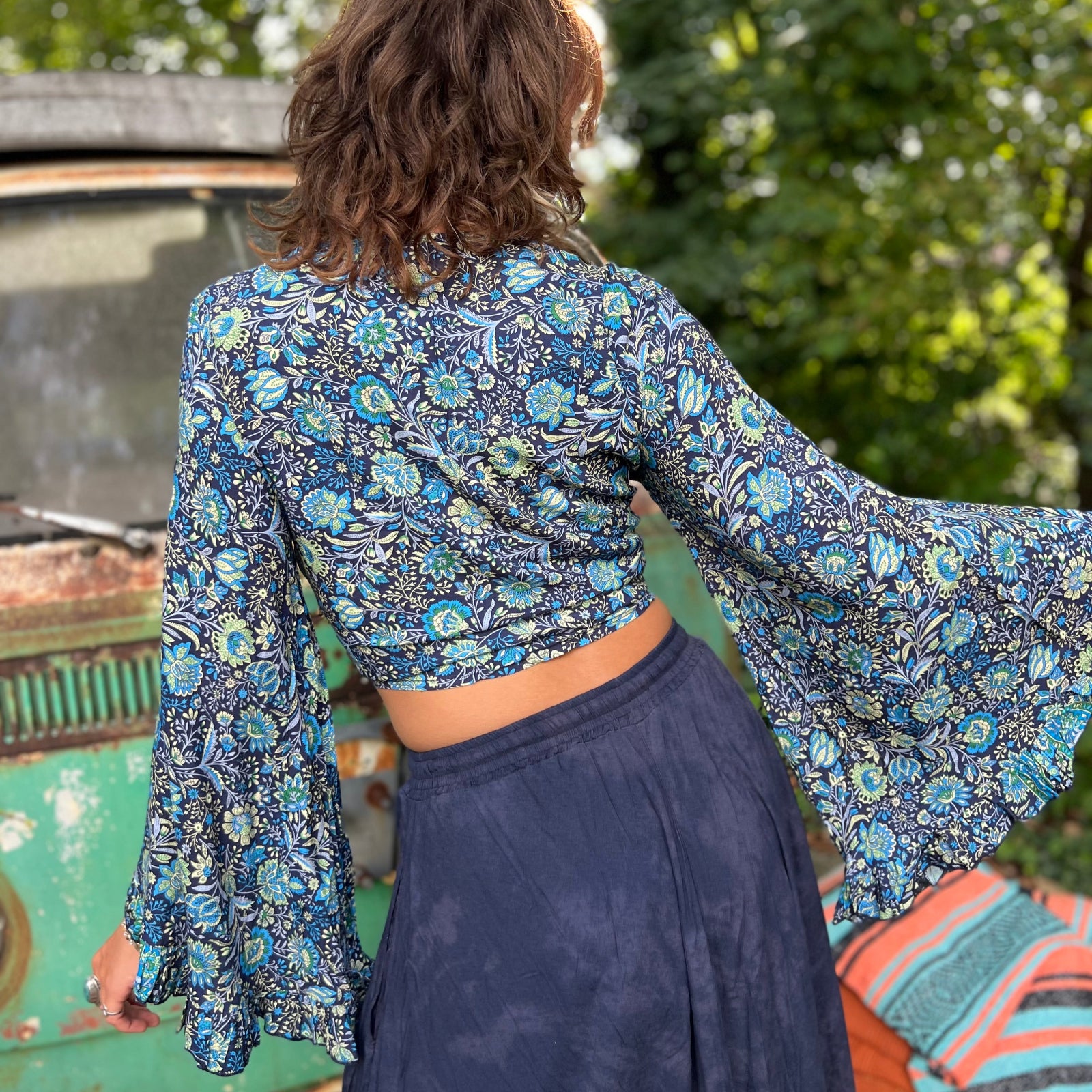 A woman wearing the blue Hippie Bohemian Bell Sleeve Wrap Top with black pants in front of a rusted vintage Volkswagen bus.