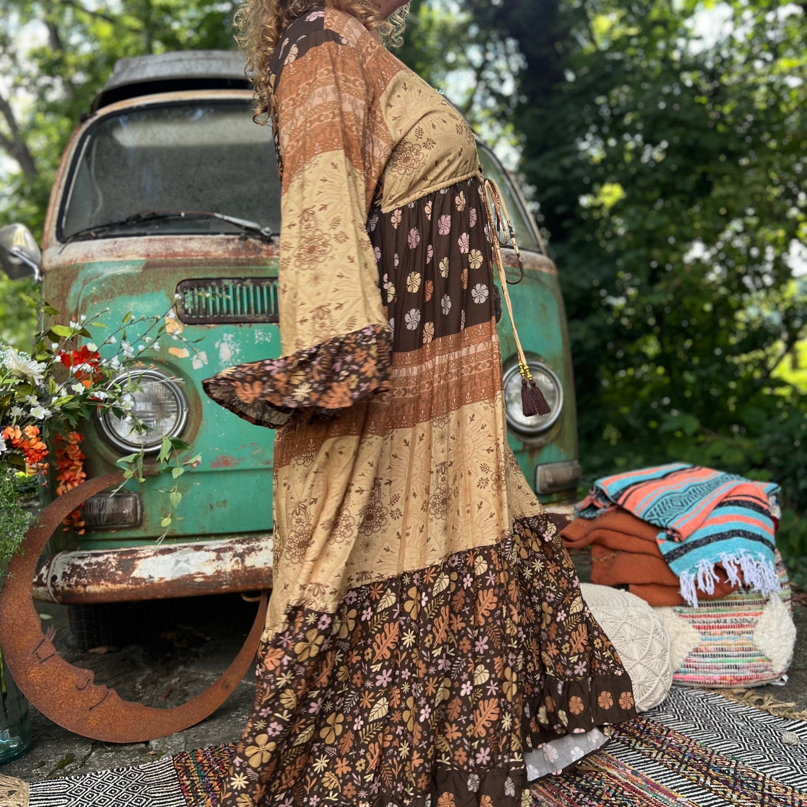 A woman wearing the Earthy Solstice Boho Bell Sleeve Maxi Dress in front of a vintage Volkswagen bus.