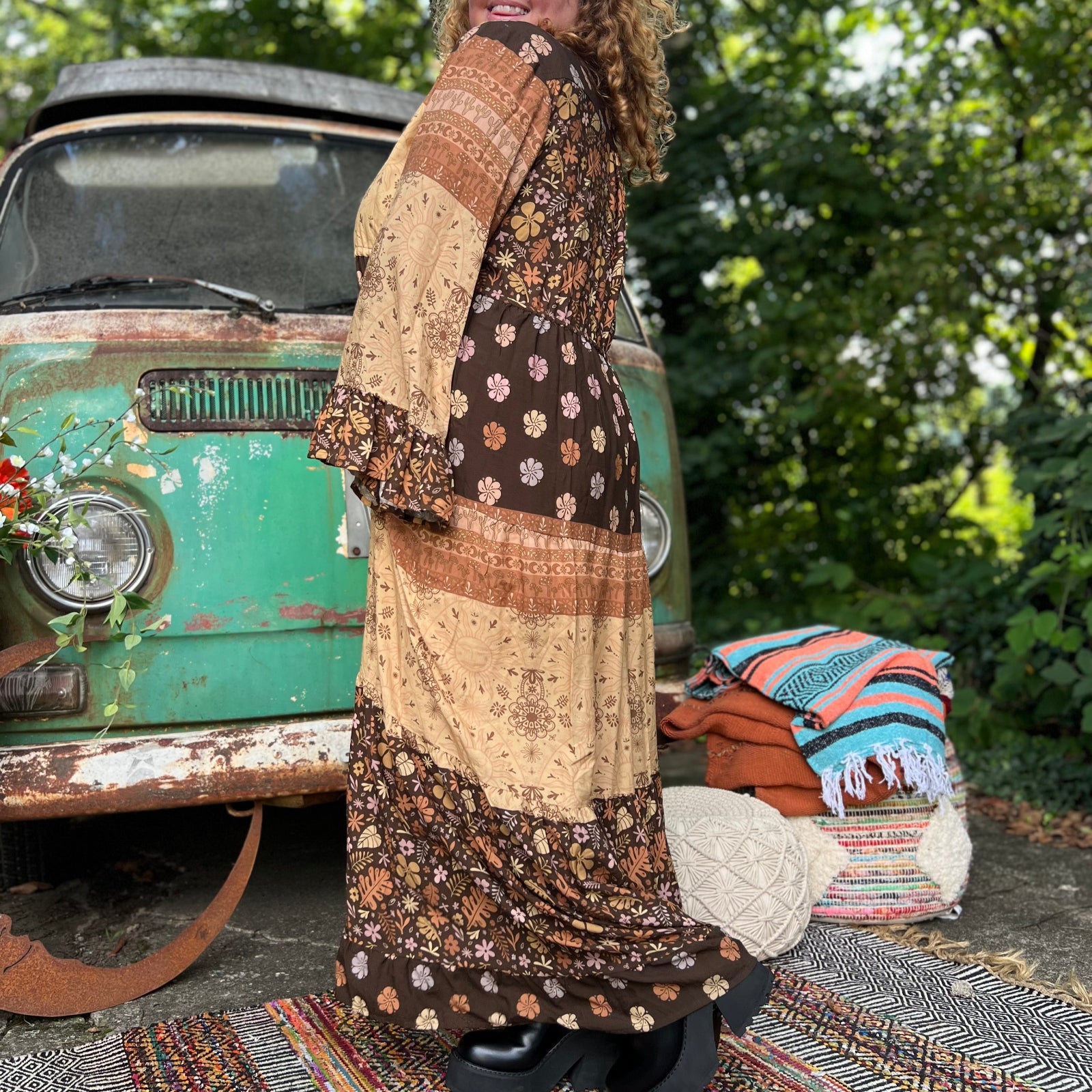 A woman wearing the Earthy Solstice Boho Bell Sleeve Maxi Dress in front of a vintage Volkswagen bus.