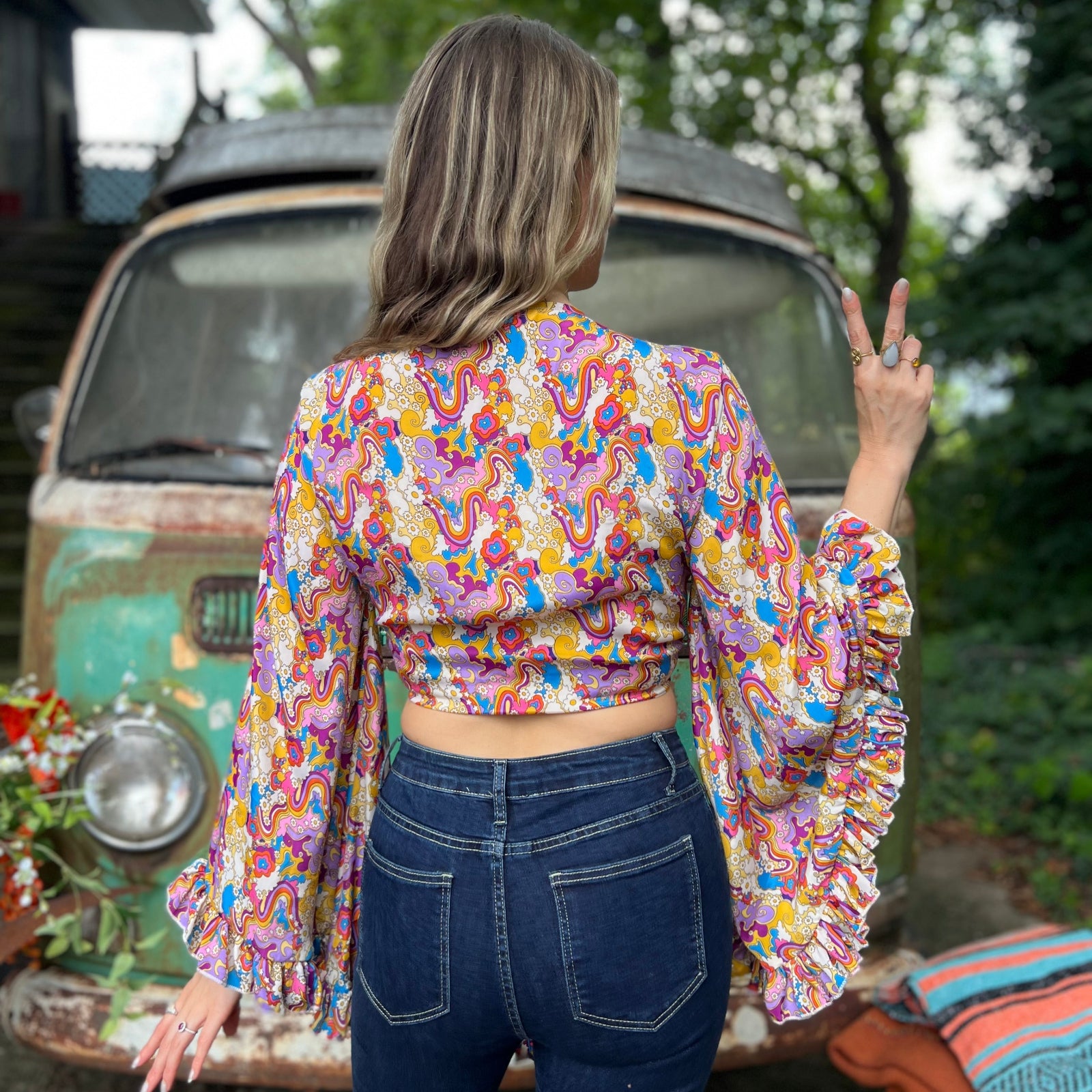 A woman wearing the rainbow Hippie Bohemian Bell Sleeve Wrap Top with black pants in front of a rusted vintage Volkswagen bus.