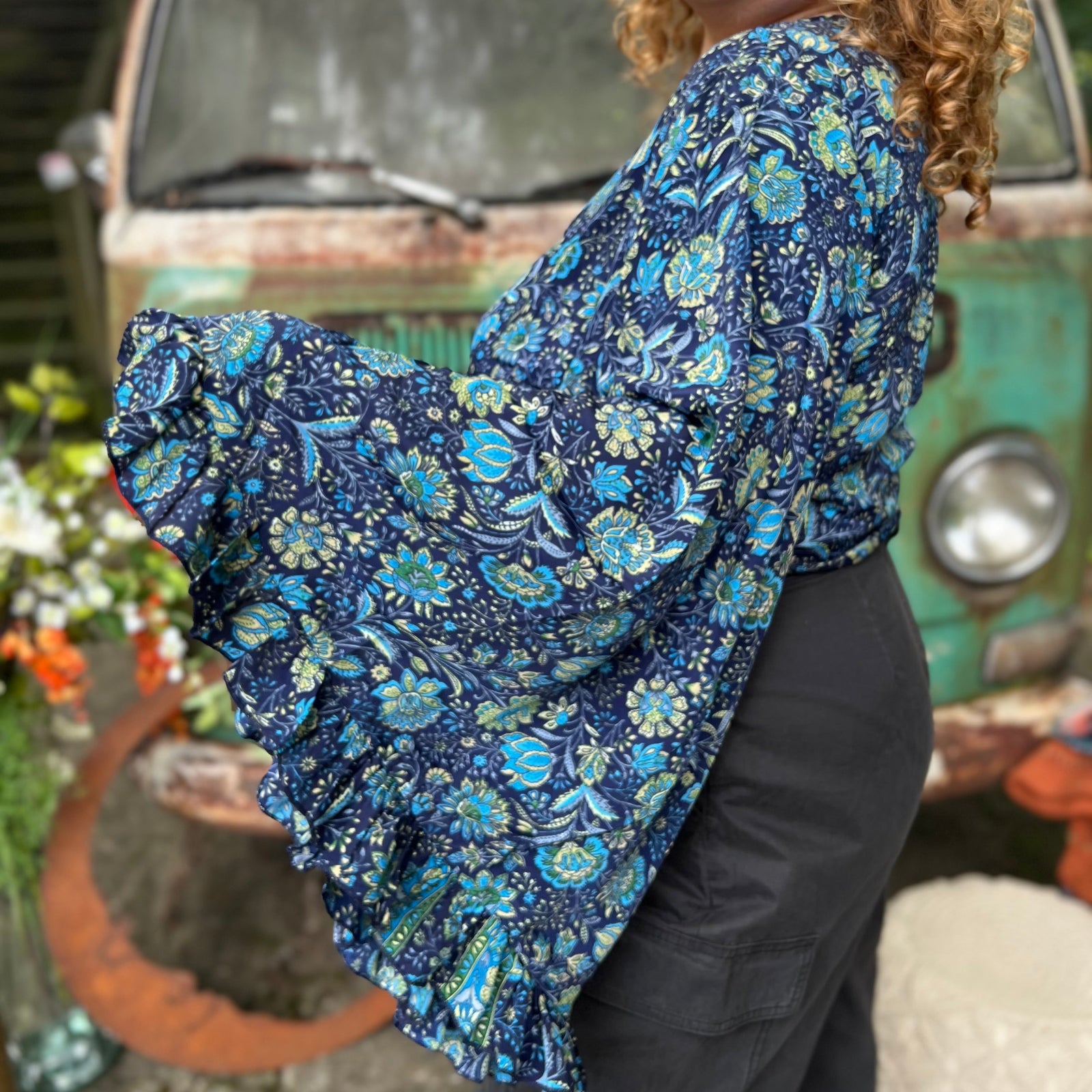 A woman wearing the blue Hippie Bohemian Bell Sleeve Wrap Top with black pants in front of a rusted vintage Volkswagen bus.