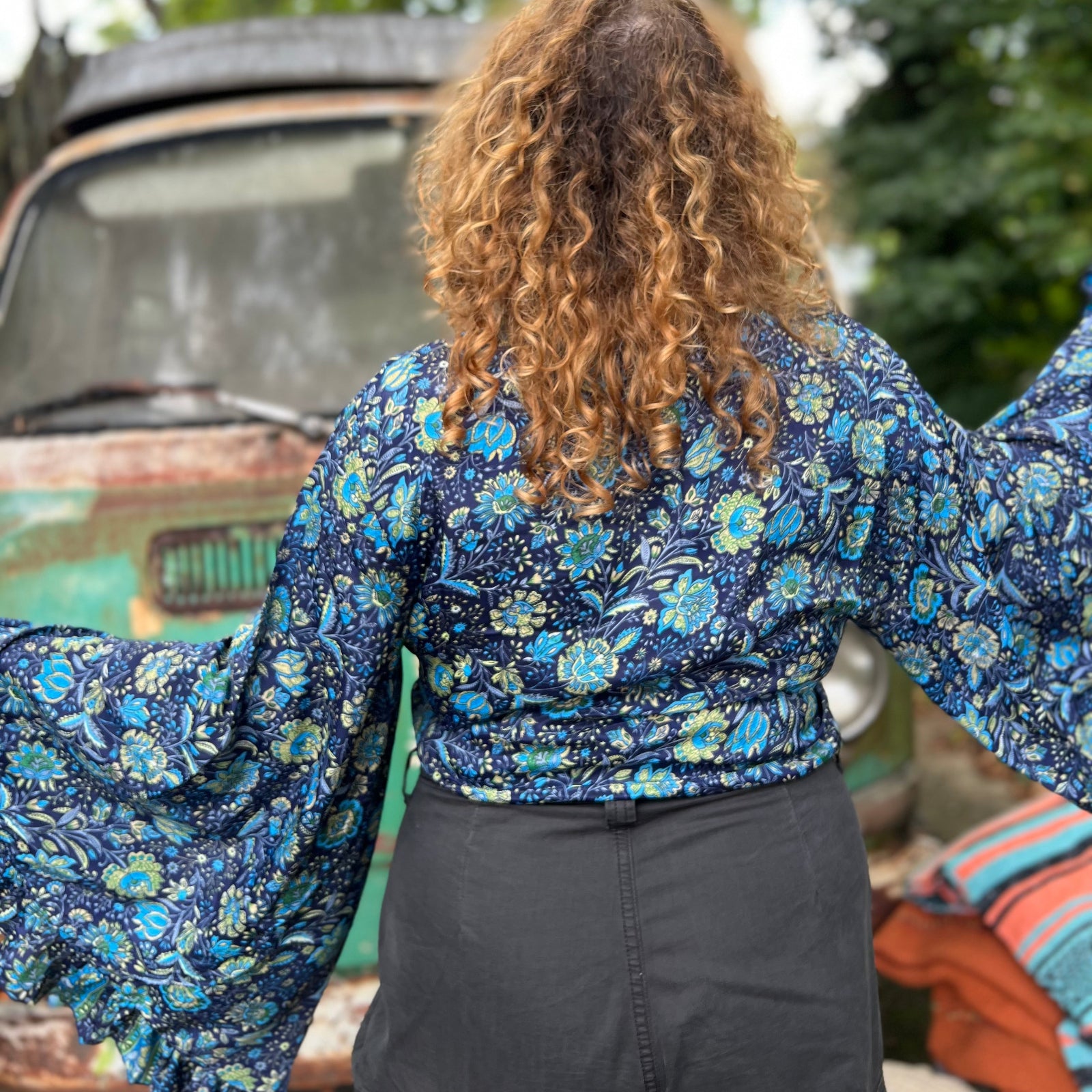 A woman wearing the blue Hippie Bohemian Bell Sleeve Wrap Top with black pants in front of a rusted vintage Volkswagen bus.