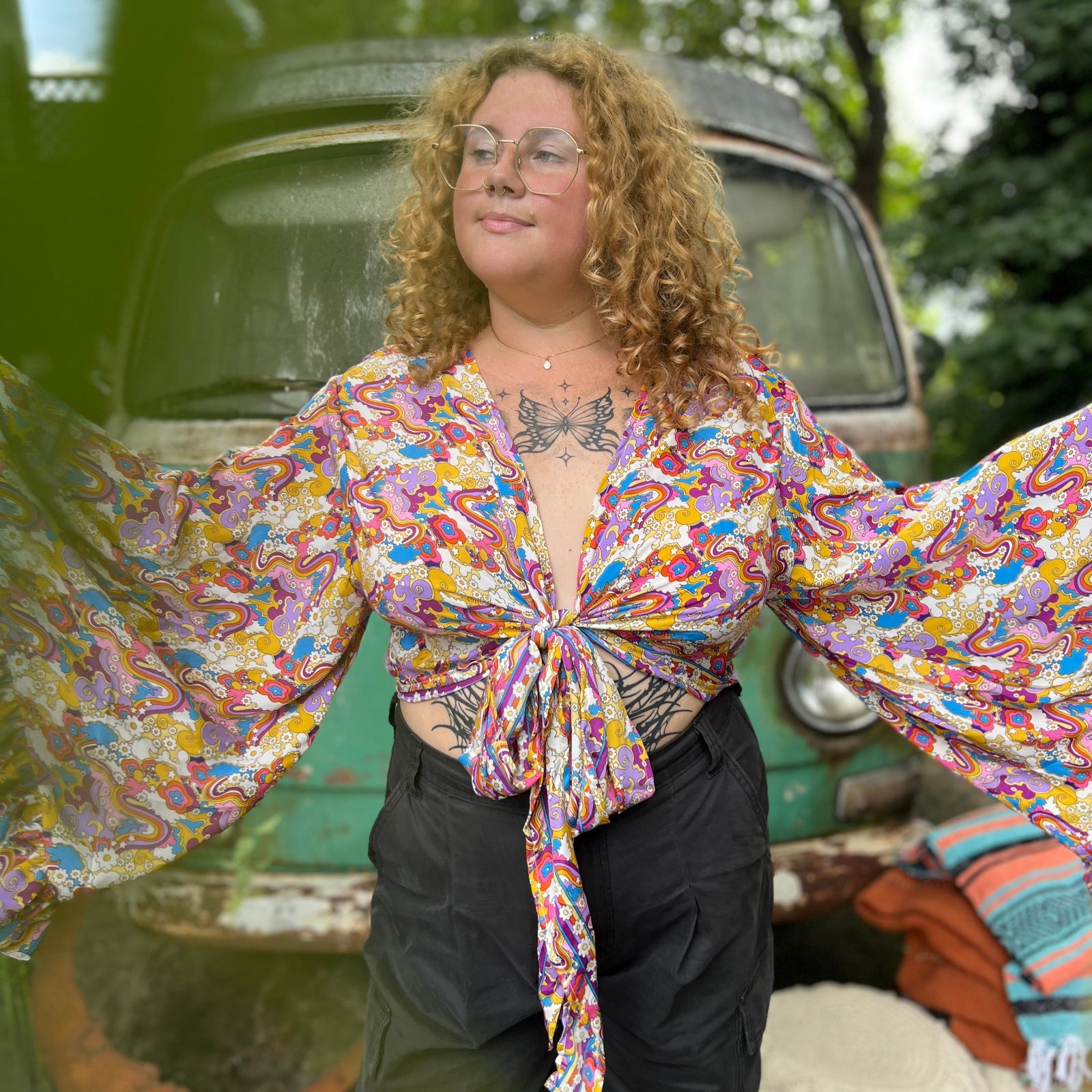 A woman wearing the rainbow Hippie Bohemian Bell Sleeve Wrap Top with black pants in front of a rusted vintage Volkswagen bus.