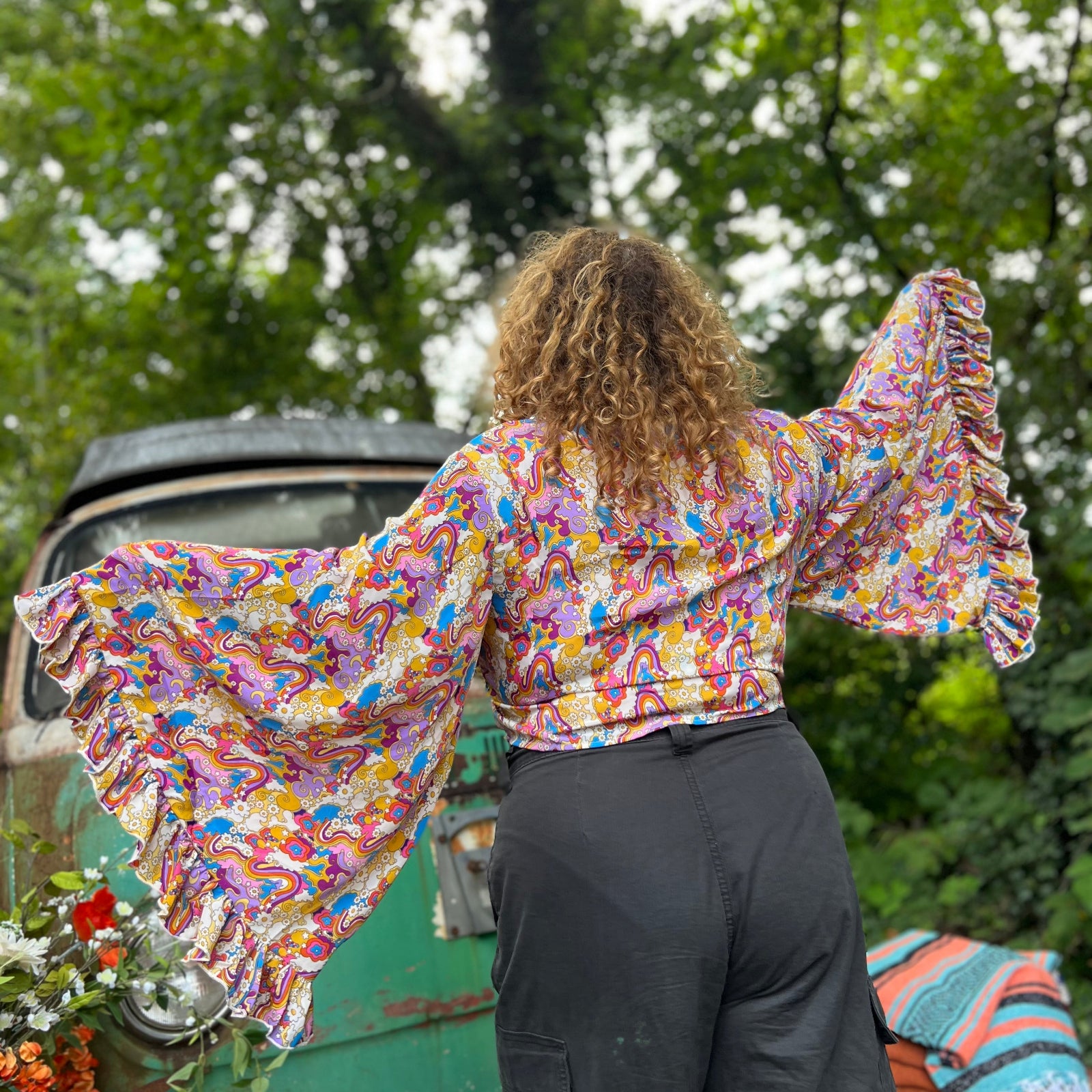 A woman wearing the rainbow Hippie Bohemian Bell Sleeve Wrap Top with black pants in front of a rusted vintage Volkswagen bus.