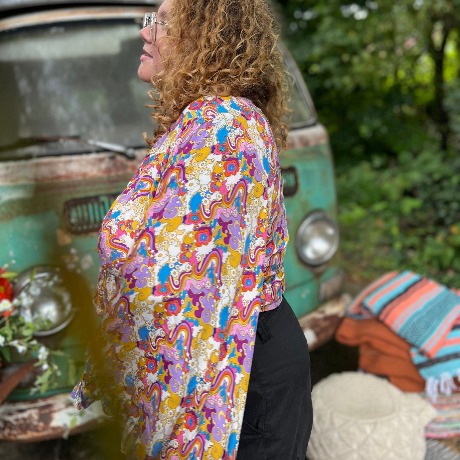 A woman wearing the rainbow Hippie Bohemian Bell Sleeve Wrap Top with black pants in front of a rusted vintage Volkswagen bus.