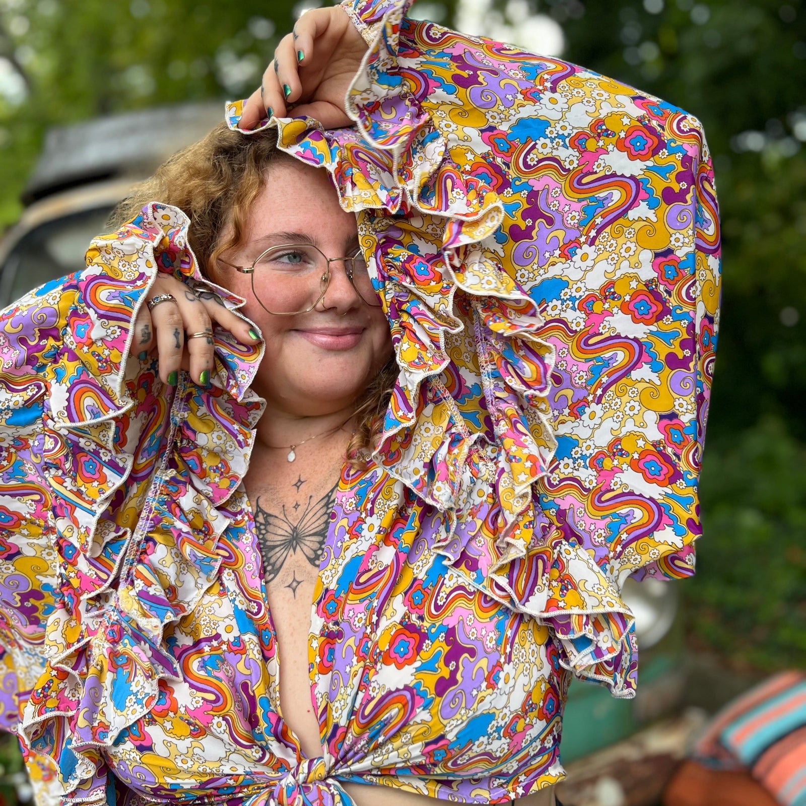 A woman wearing the rainbow Hippie Bohemian Bell Sleeve Wrap Top with black pants in front of a rusted vintage Volkswagen bus.