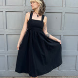 A woman wearing the Black Woven Polyester Nylon Back Cross Strap Midi Dress with sandals and a black crystal necklace.