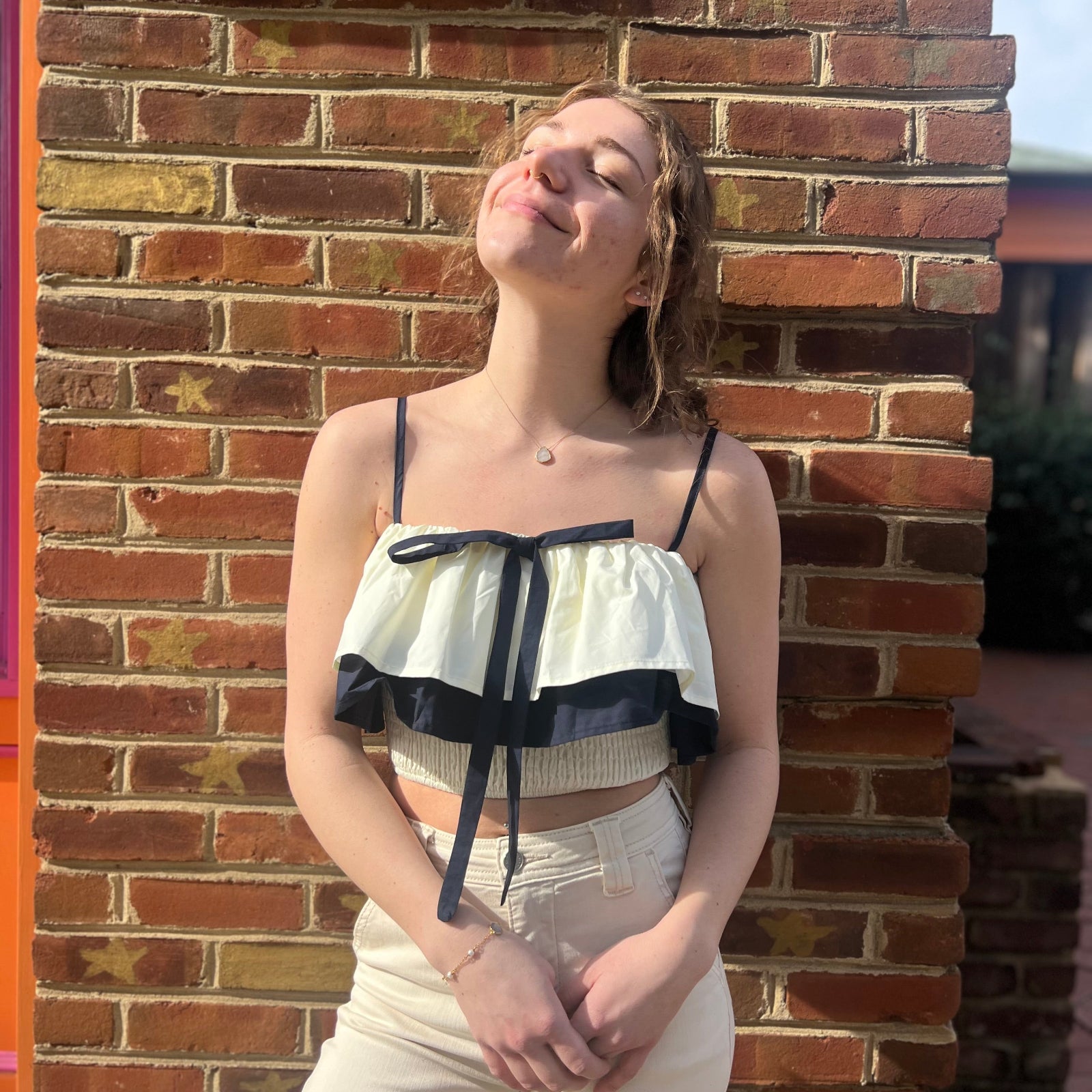 A woman wearing the Contrast Cotton Flare Bow Top with white jeans in front of a brick wall.