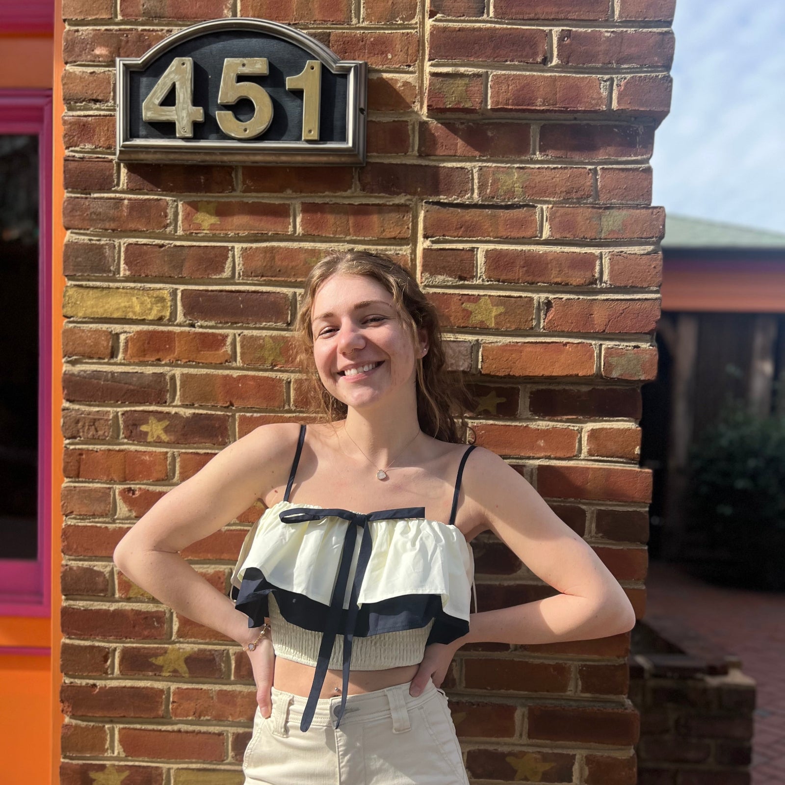 A woman wearing the Contrast Cotton Flare Bow Top with white jeans in front of a brick wall.