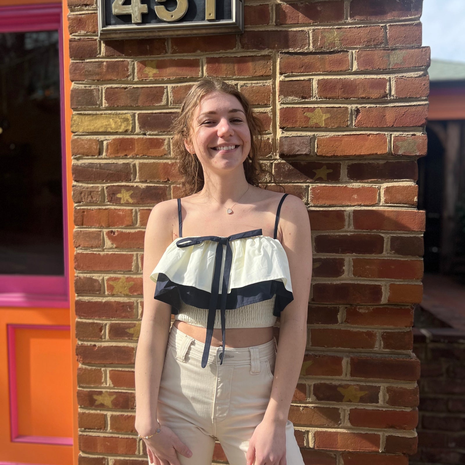 A woman wearing the Contrast Cotton Flare Bow Top with white jeans in front of a brick wall.