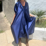 A woman wearing the Shadow Caftan with a pair of brown boots in front of a white building.