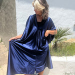 A woman wearing the Shadow Caftan with a pair of brown boots in front of a white building.