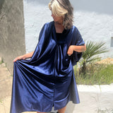 A woman wearing the Shadow Caftan with a pair of brown boots in front of a white building.