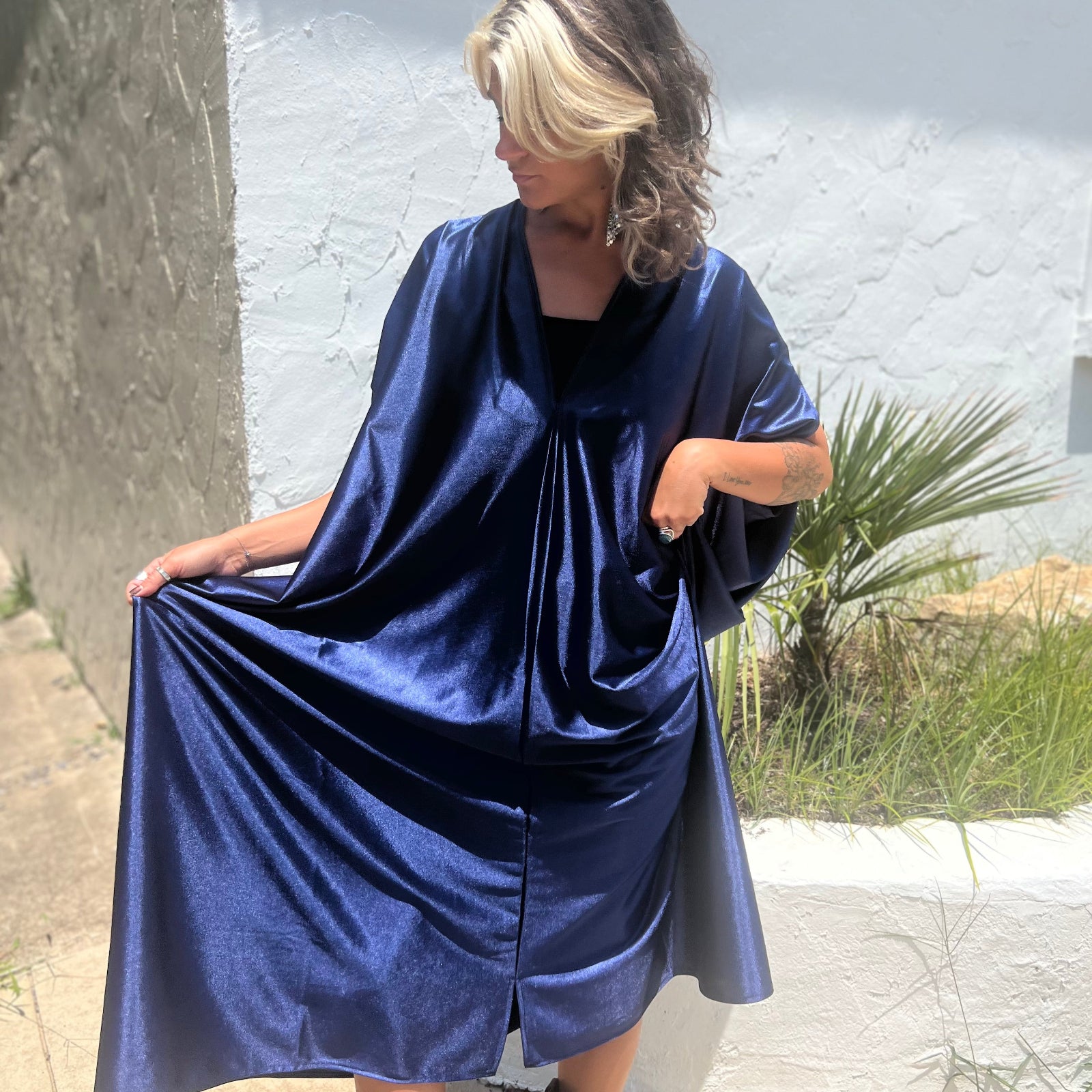 A woman wearing the Shadow Caftan with a pair of brown boots in front of a white building.
