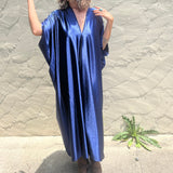 A woman wearing the Shadow Caftan with a pair of brown boots in front of a white building.