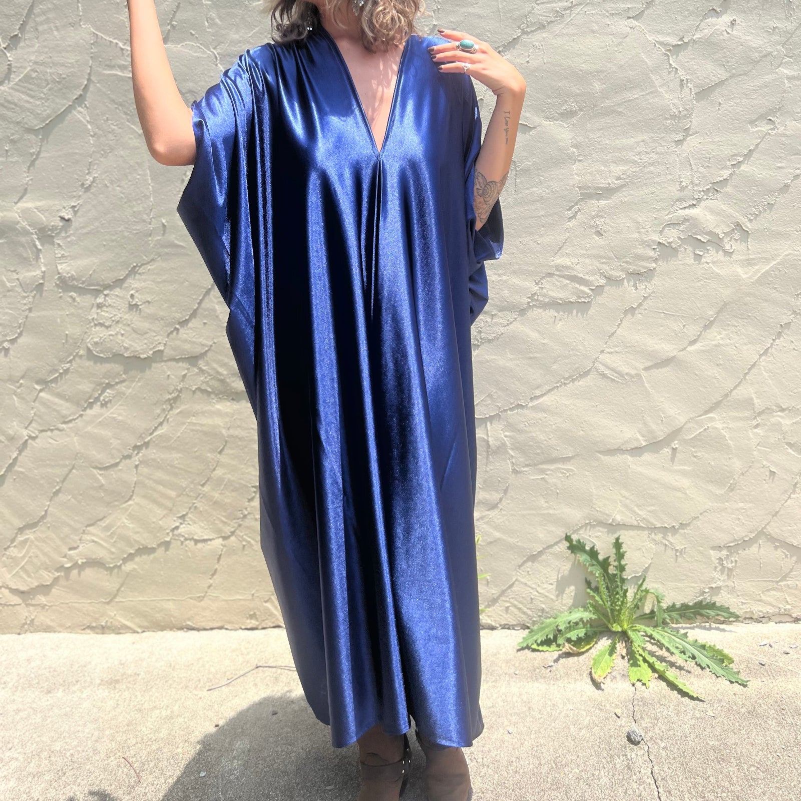 A woman wearing the Shadow Caftan with a pair of brown boots in front of a white building.