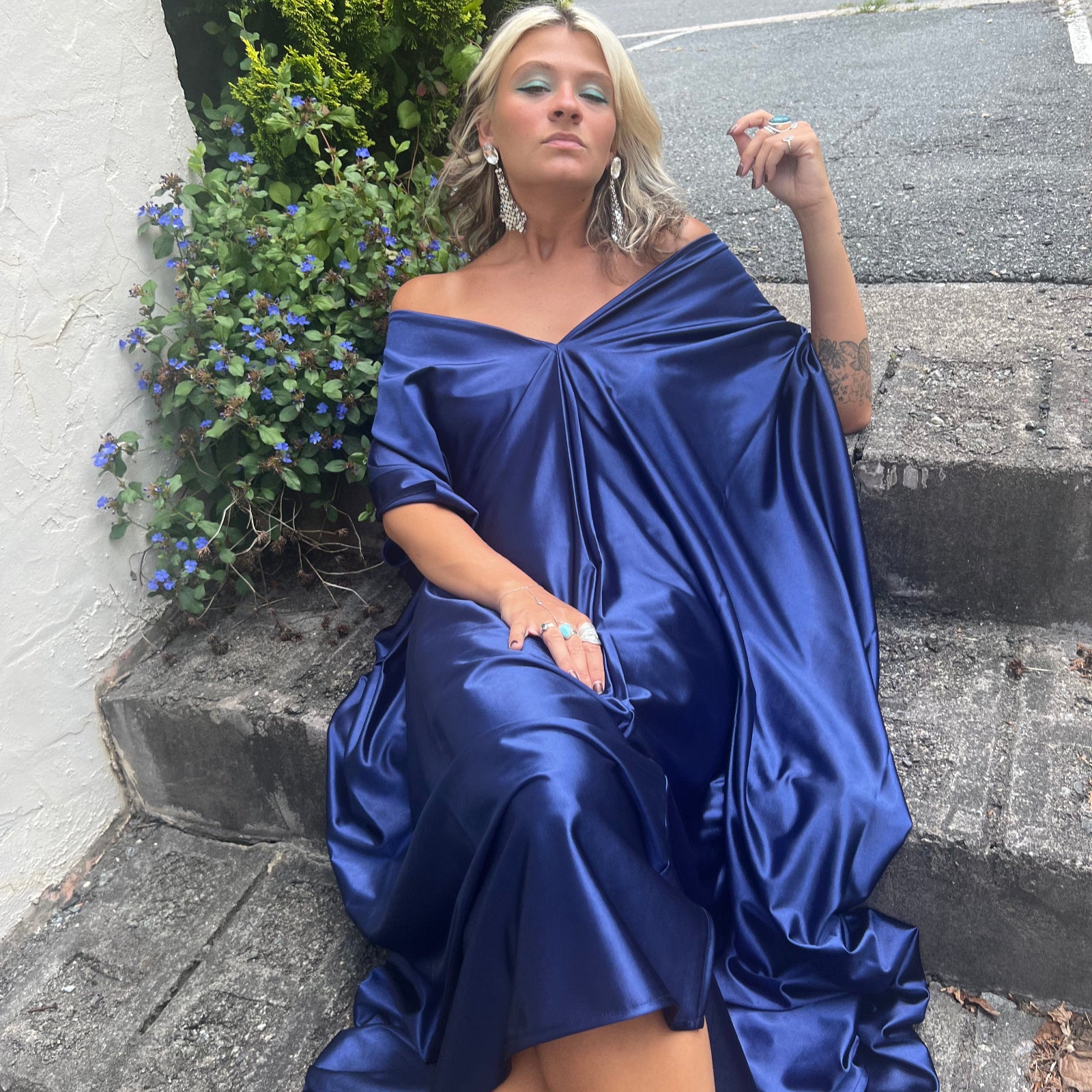 A woman wearing the Shadow Caftan while sitting on some concrete stairs.