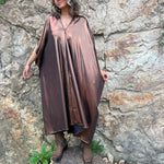 A woman wearing the Chiara Caftan in front of a stone wall.