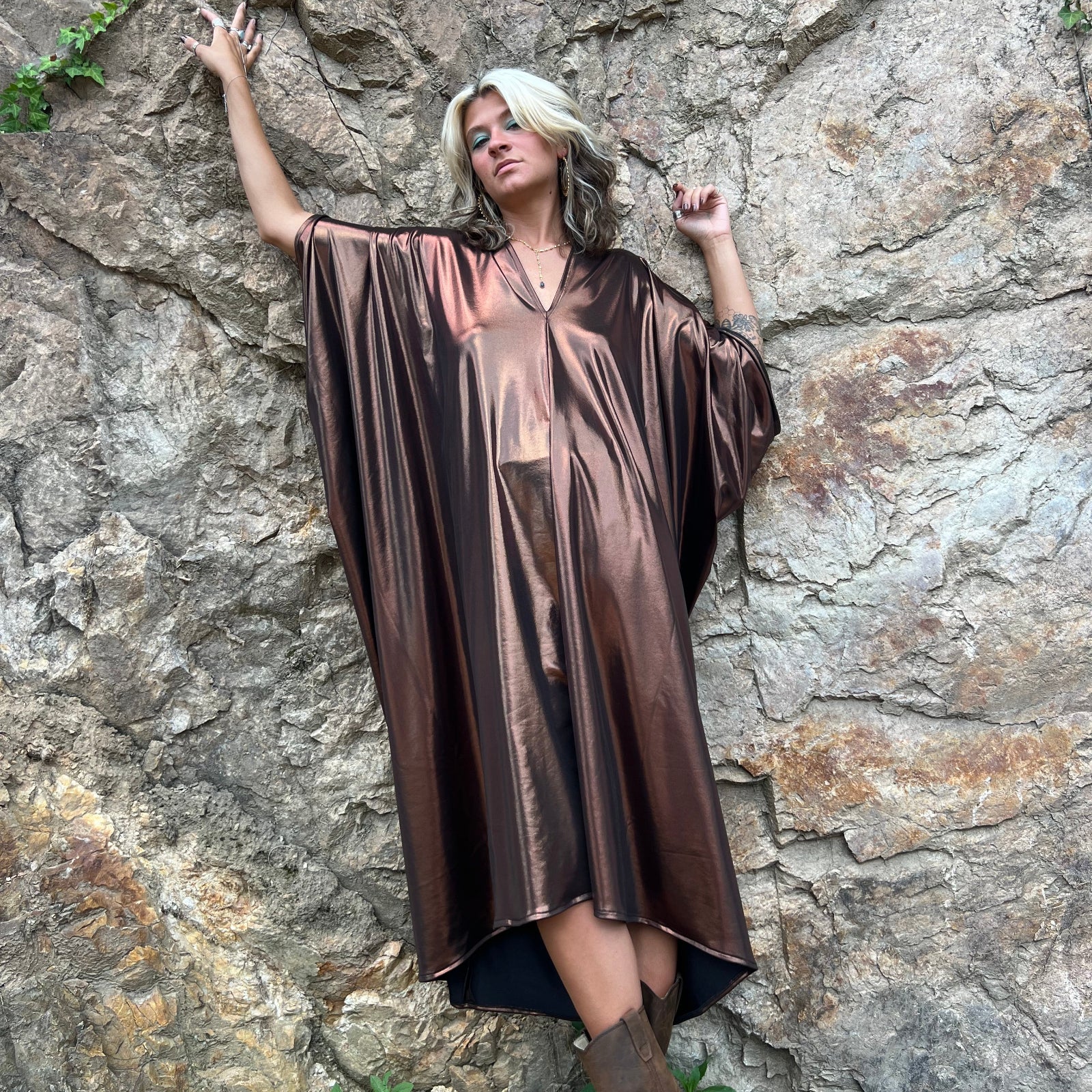 A woman wearing the Chiara Caftan in front of a stone wall.