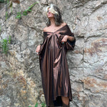 A woman wearing the Chiara Caftan in front of a stone wall.