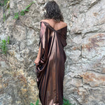 A woman wearing the Chiara Caftan in front of a stone wall.