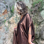 A woman wearing the Chiara Caftan in front of a stone wall.