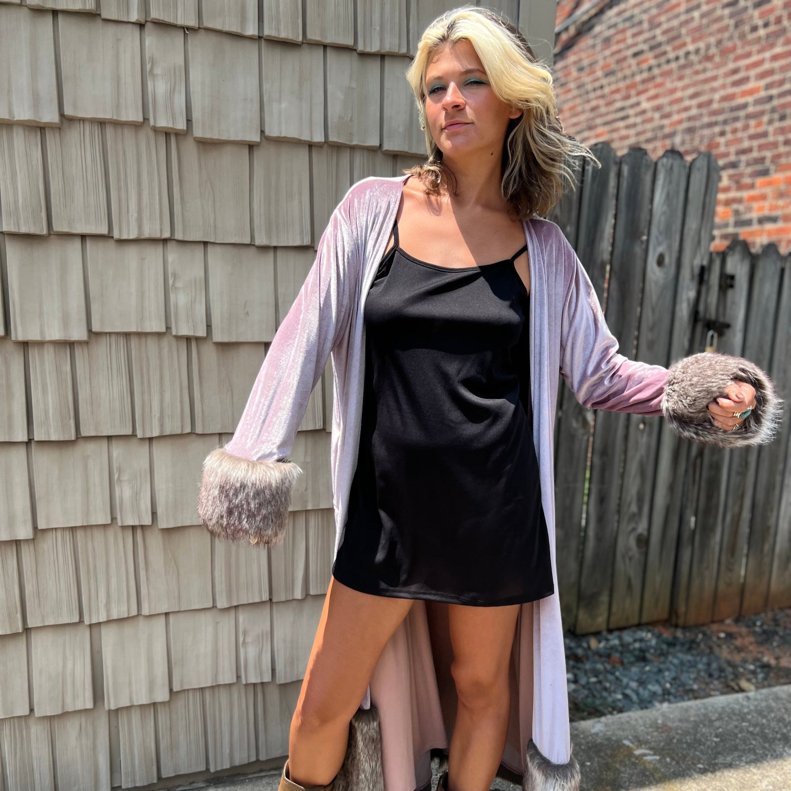 A woman wearing the Blush Velvet Faux Fur Jacket by Jennafer Grace with a black dress and brown boots.