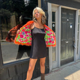 A woman wearing the Planet Queen Orange Faux Fur Jacket with a black dress in front of a window.