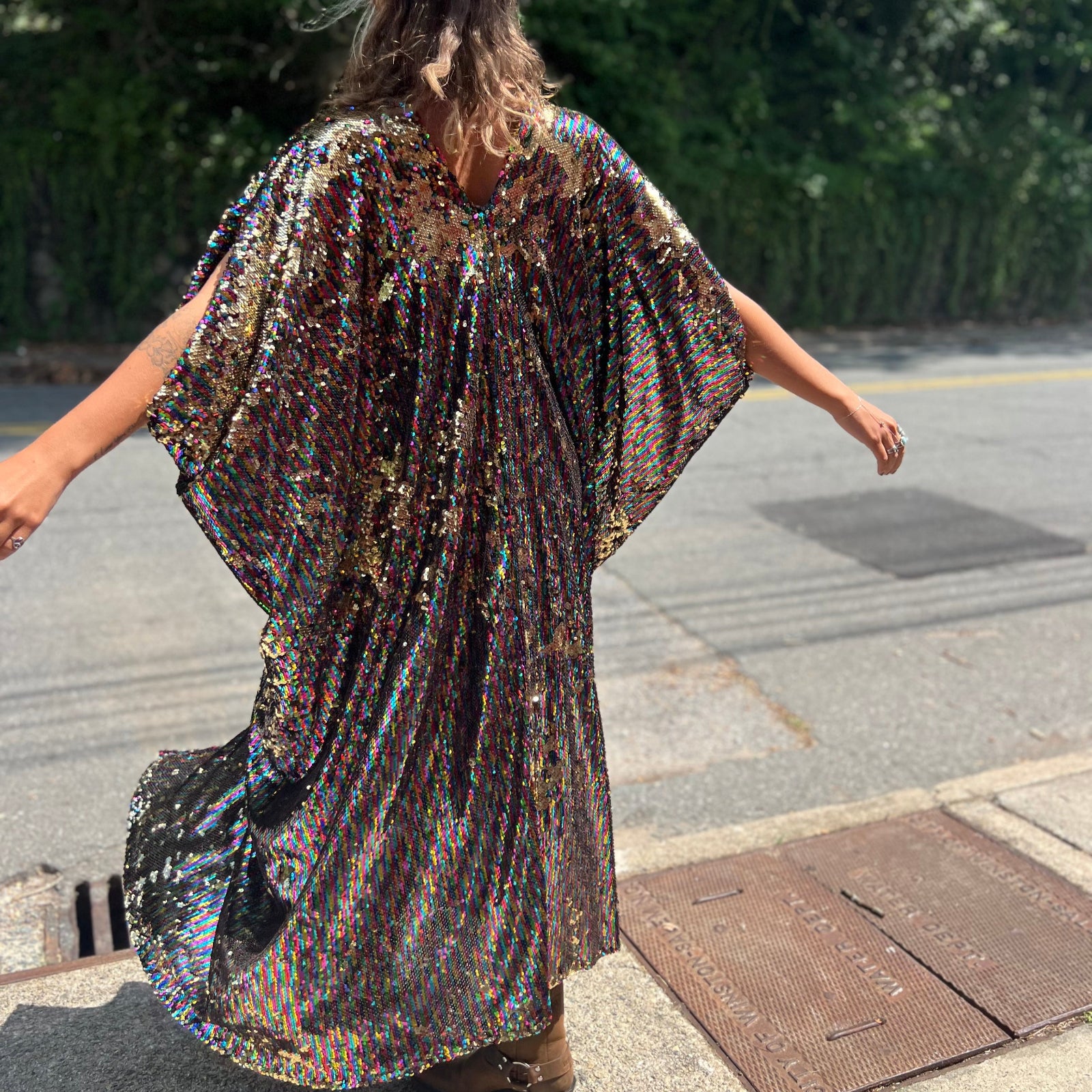 A woman wearing the Rainbow Rage Sequin Caftan with a black dress and brown boots.