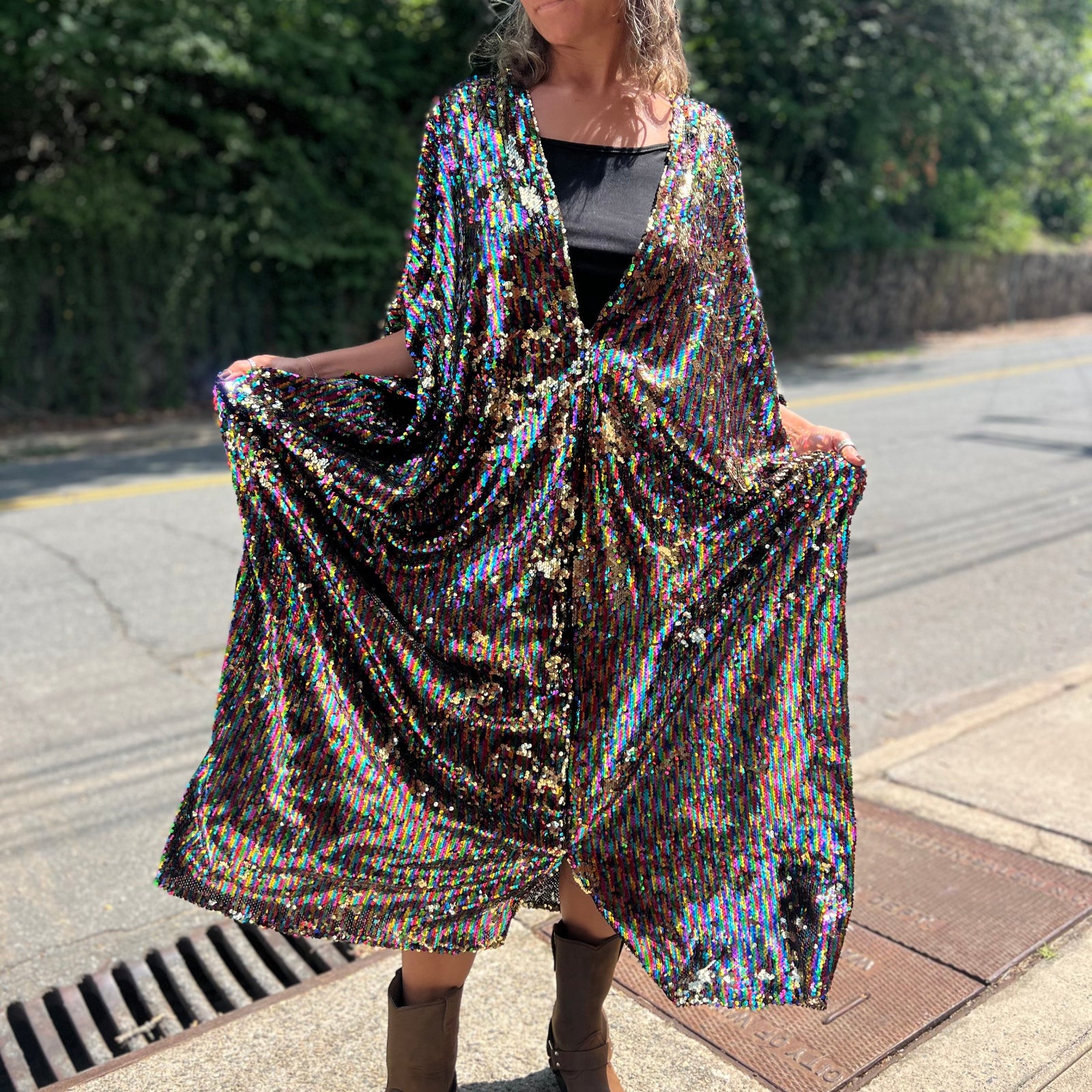A woman wearing the Rainbow Rage Sequin Caftan with a black dress and brown boots.