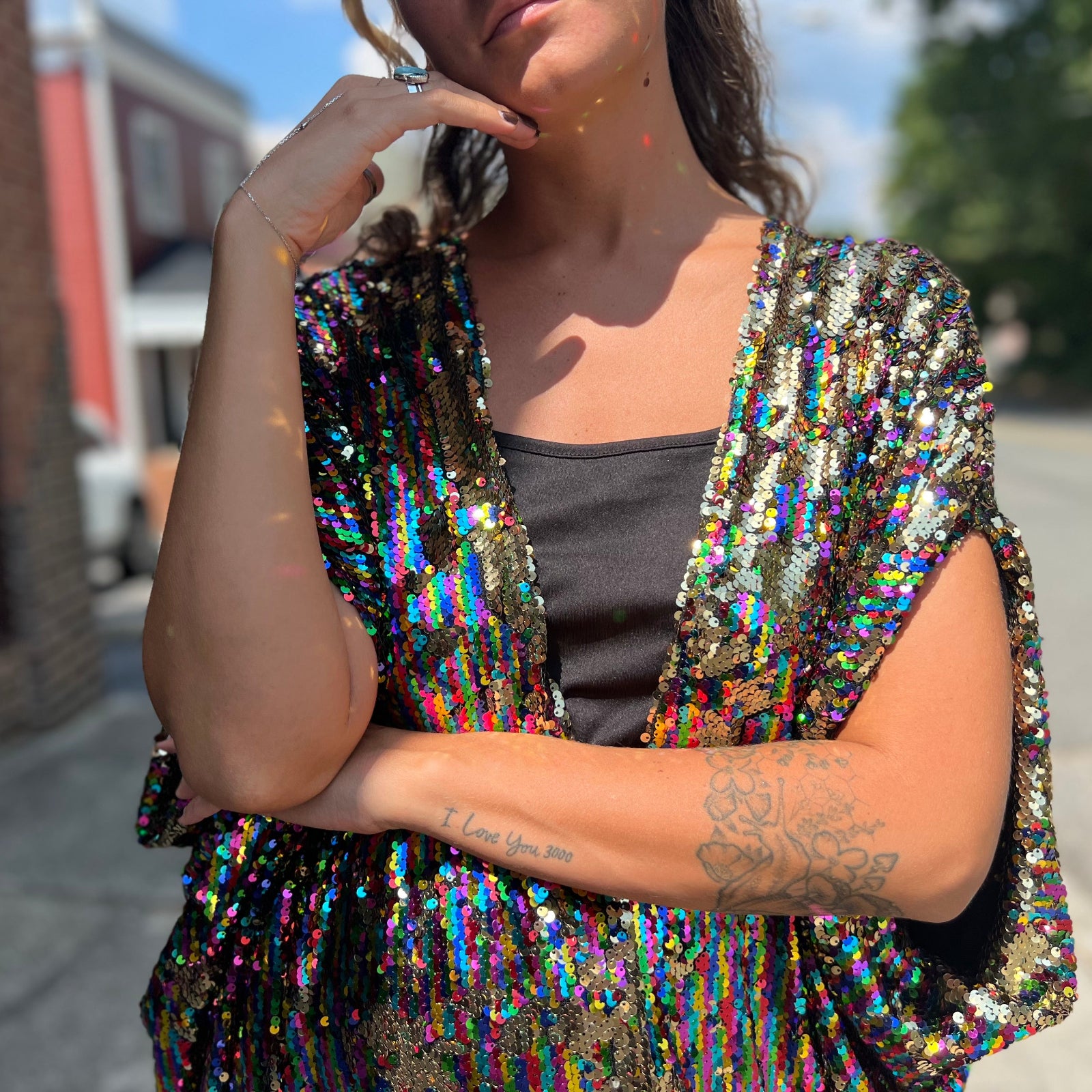 A woman wearing the Rainbow Rage Sequin Caftan with a black dress and brown boots.