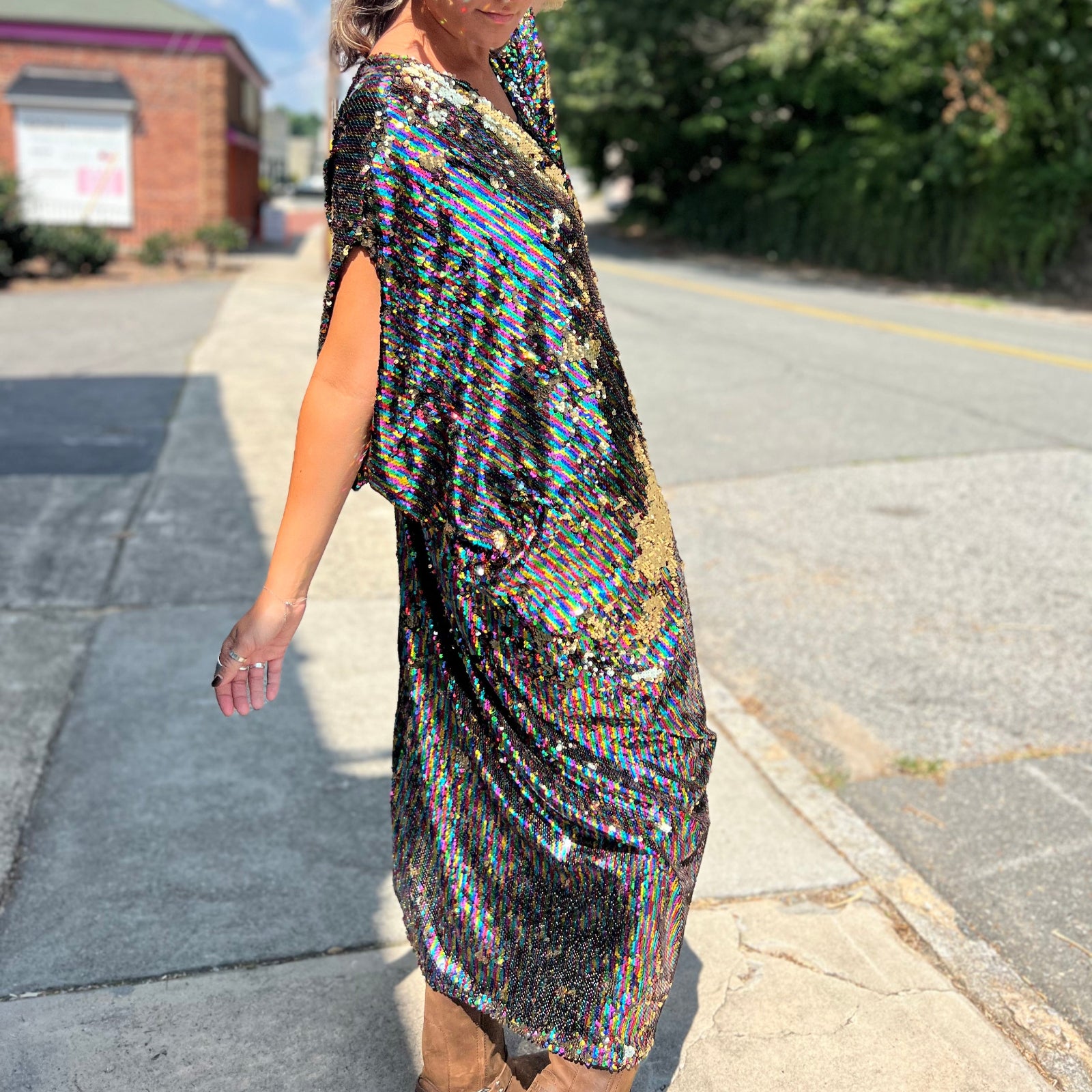 A woman wearing the Rainbow Rage Sequin Caftan with a black dress and brown boots.