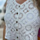 A woman wearing the white V-Neck Crochet Button Up Vest with beige linen pants.