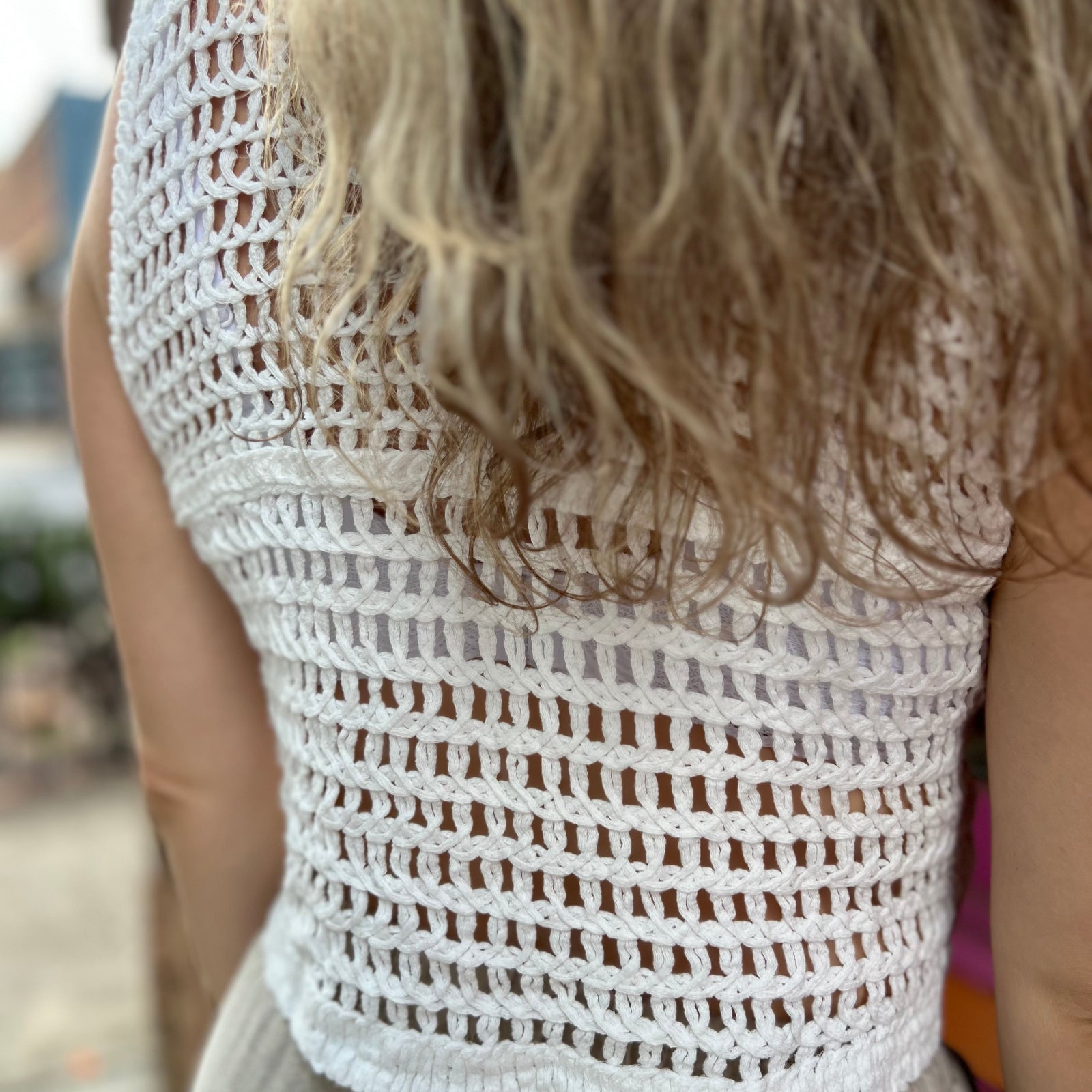 A woman wearing the white V-Neck Crochet Button Up Vest with beige linen pants.
