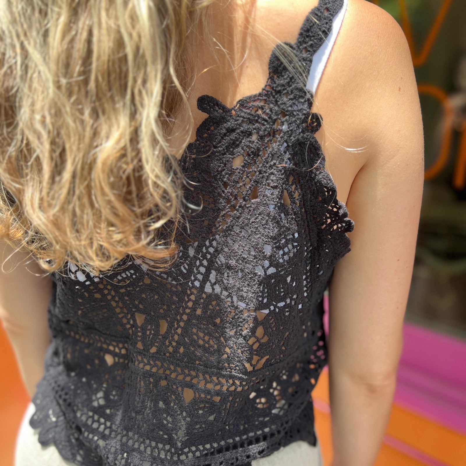 A woman wearing the black Solid Color Crochet Lace Hollow Camisole Top with beige linen pants.