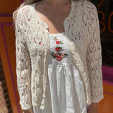 A woman wearing the Diamond Crochet Cardigan with a white dress.
