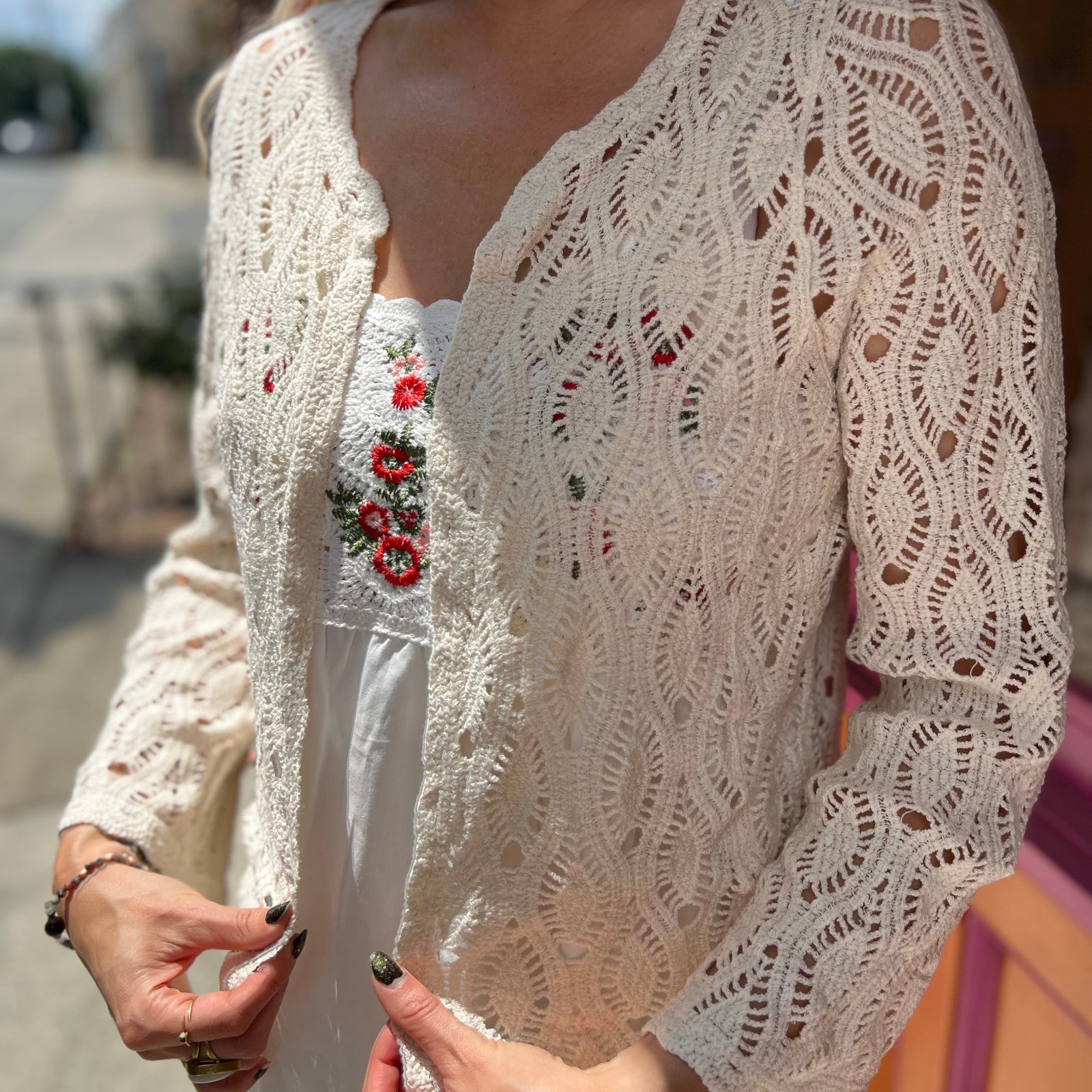 A woman wearing the Diamond Crochet Cardigan with a white dress.