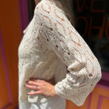 A woman wearing the Diamond Crochet Cardigan with a white dress.
