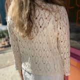 A woman wearing the Diamond Crochet Cardigan with a white dress.